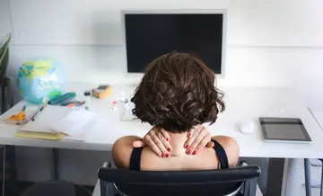 Frau am Schreibtisch massiert sich den Nacken