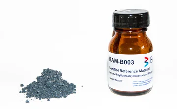 Braunes Glasfläschchen mit Schraubverschluss und Etikett neben grauem Pulverhaufen