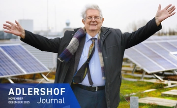 Klaus Thiessen joyfully raising his arms in front of solar panels