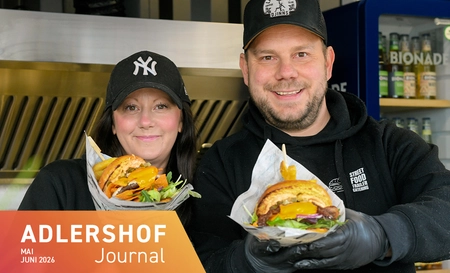 Mann und Frau mit Basecaps halten reich belegte Burger in den Händen