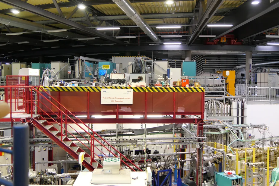 Experimental hall with machinery, pipes and a red metal staircase leading up to a raised platform