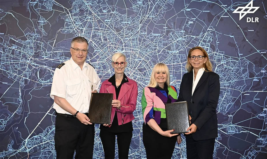 Vier Personen mit Dokumentmappen vor einer Berlin-Karte mit DLR-Logo