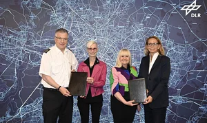 Vier Personen mit Dokumentmappen vor einer Berlin-Karte mit DLR-Logo