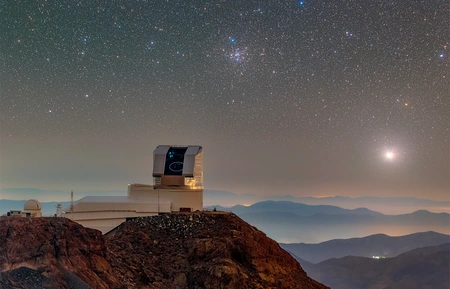 Das Observatorium mit geöffneter Kuppel auf einem Berggipfel in den chilenischen Anden bei Nacht mit klarem Sternenhimmel im Hintergrund.