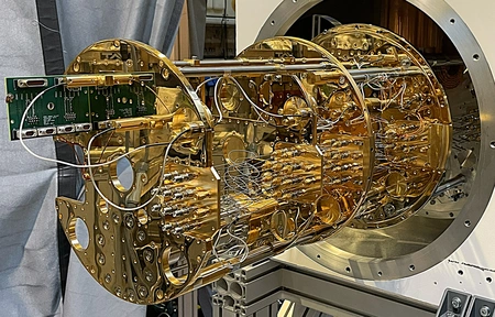 A gold-coloured cryostat with numerous wires and cables, housed in a large, round casing