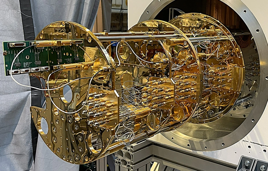 A gold-coloured cryostat with numerous wires and cables, housed in a large, round casing