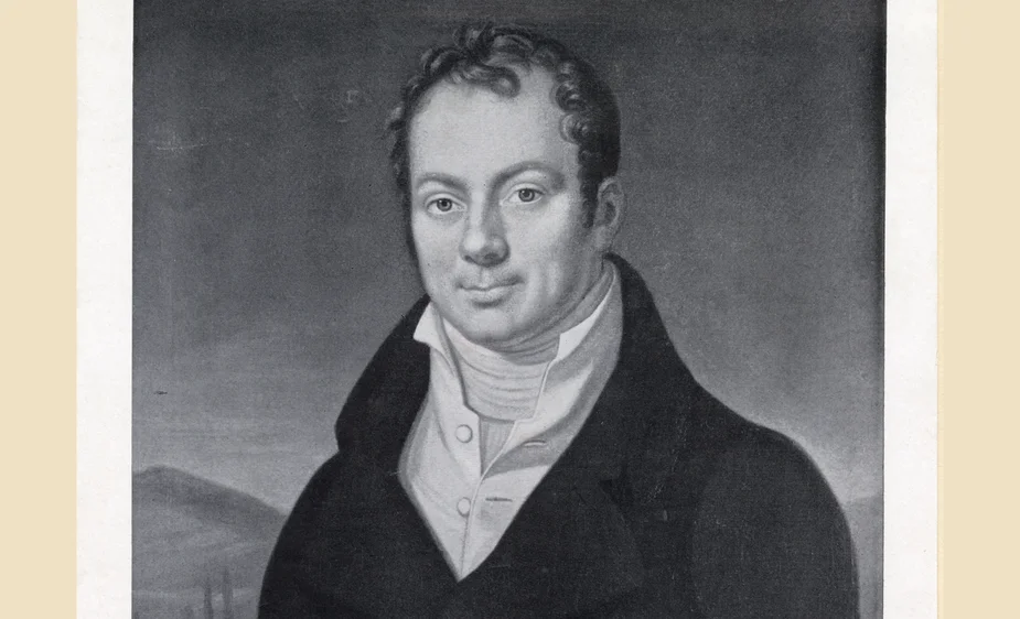 Portrait of a man in a dark suit and white shirt against a blurred background