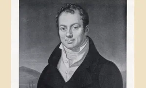 Portrait of a man in a dark suit and white shirt against a blurred background