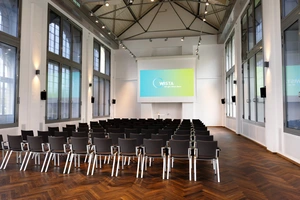 Hans-Grade-Saal with rows of chairs facing a projection screen and tall windows on the sides