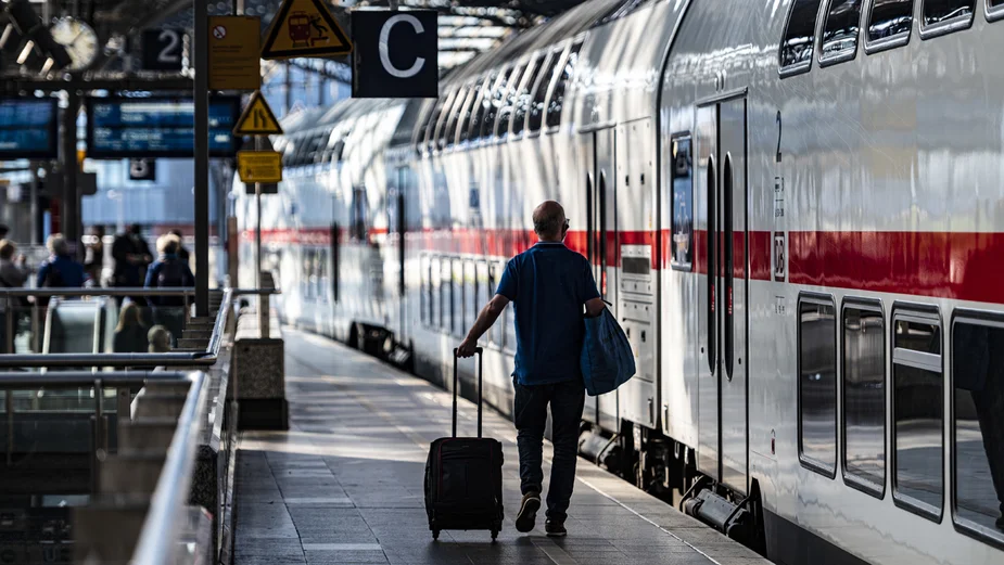 A man with a wheeled suitcase by a train