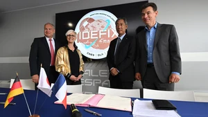 Auf dem Foto stehen die Unterzeichnenden (in der Bildbeschreibung) des Abkommens vor einem Bildschirm auf dem das IDEFIX Logo zu sehen ist.. © DLR