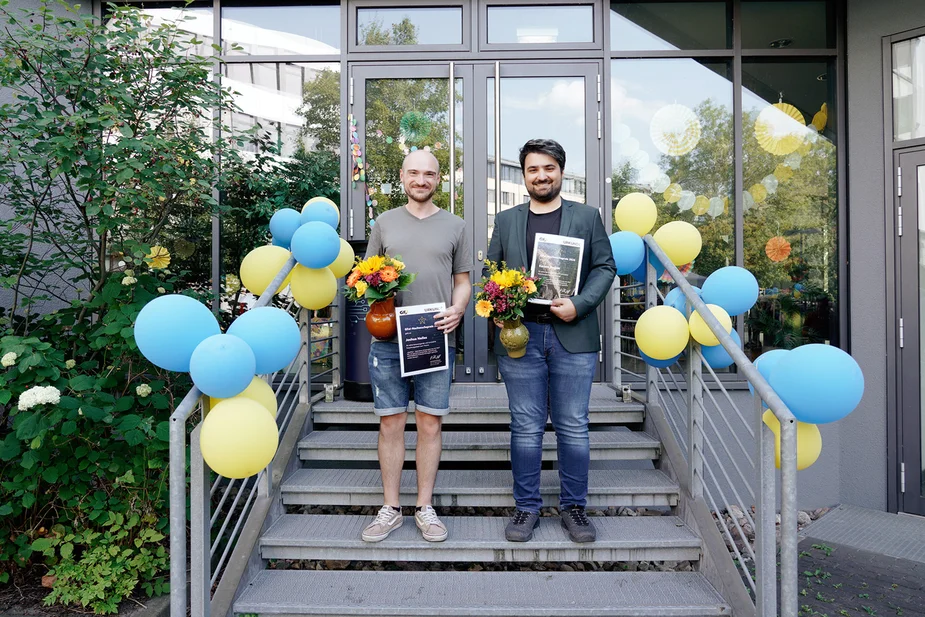 Die Gewinner mit Urkunden und Blumen vor dem geschmückten Gebäude