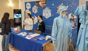 Messestand mit zwei Personen an einem Messestand mit einer Schaufensterpuppe in blauem Schutzanzug