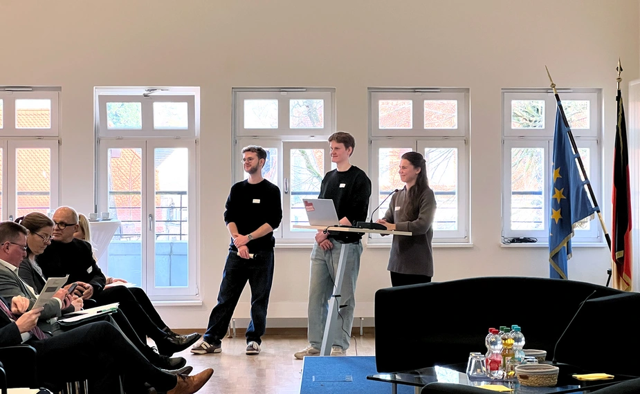 3 junge Menschen stehen am Pult vor dem Publikum