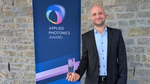 Marc Christ mit dem gläsernen Preis vor einem Banner mit der Aufschrift "Applied Photonics Award"