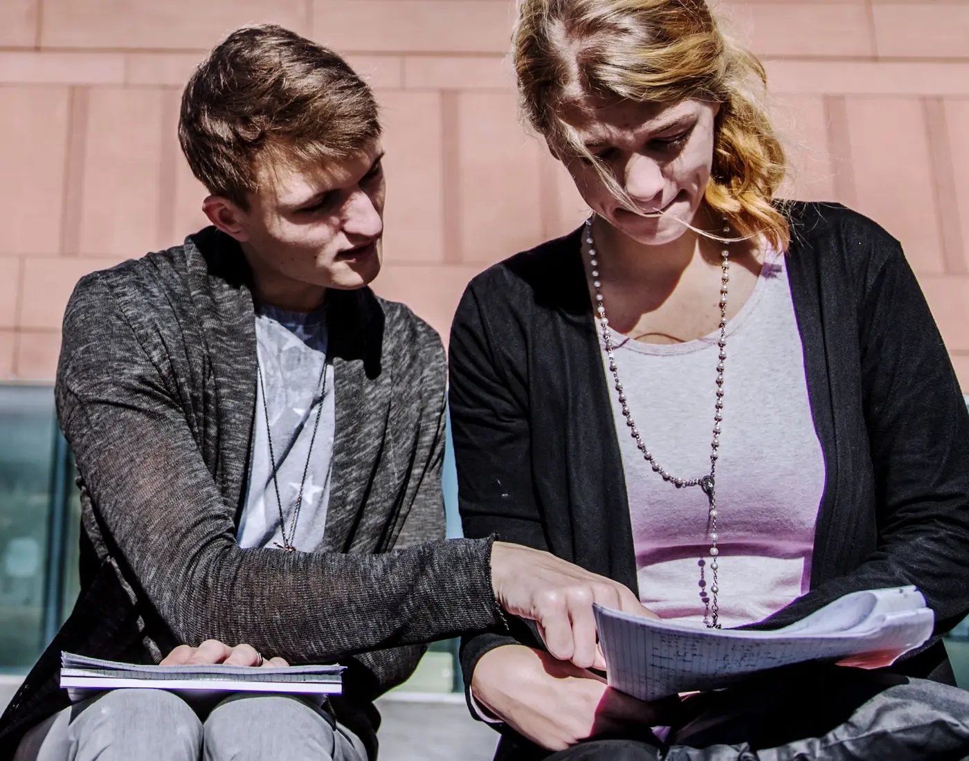 Ein Student und eine Studentin sitzen auf einer Bank und gehen gemeinsam ihre Aufzeichnungen durch